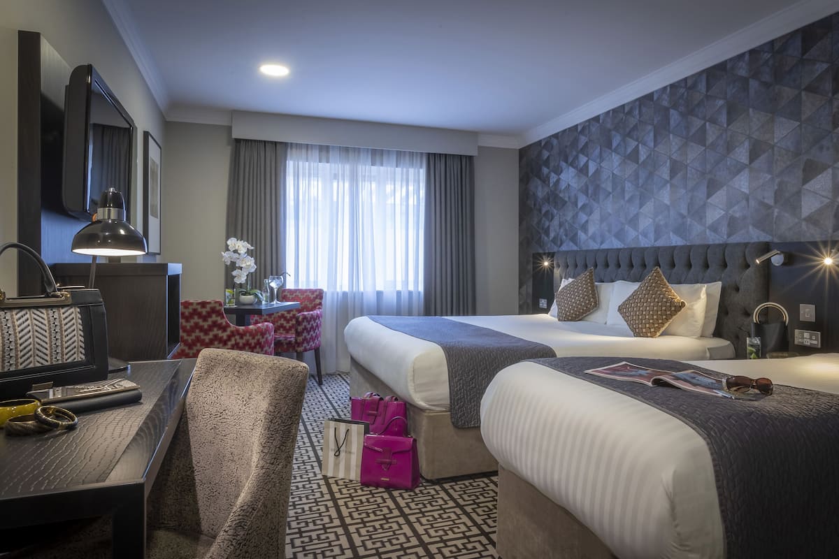 A hotel room with two beds, a desk, and a chair.