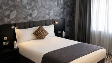 Una habitación de hotel con una cama grande, una pared con estampado geométrico, una mesita de noche con lámpara y un suelo estampado.