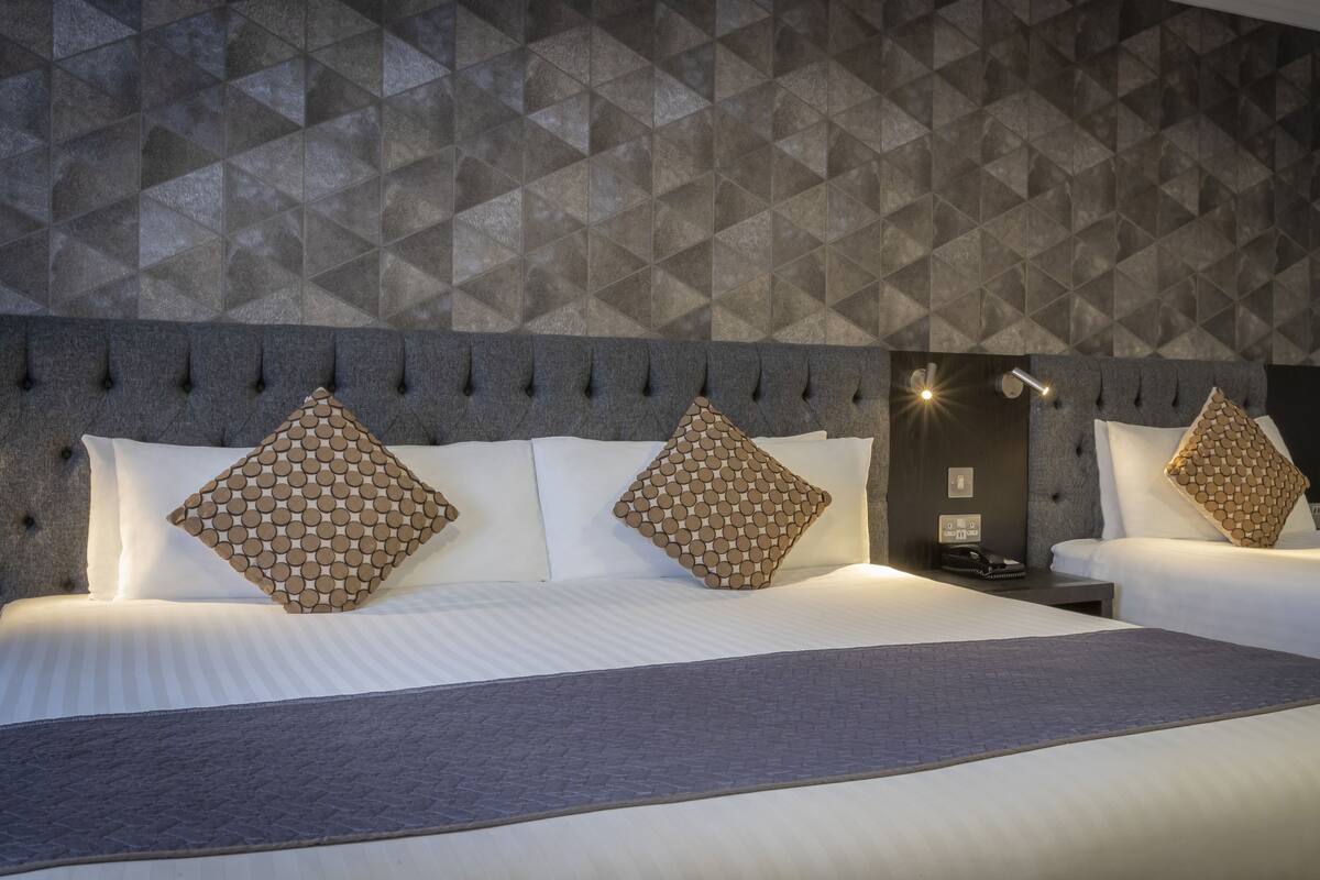 A hotel room with a geometric patterned wall, a tufted headboard, and two beds with matching pillows.