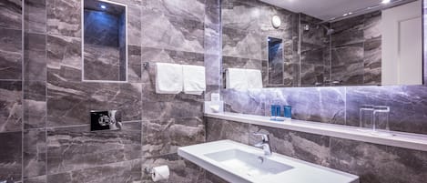 A modern bathroom with a large mirror, marble walls, a white sink, and a toilet.