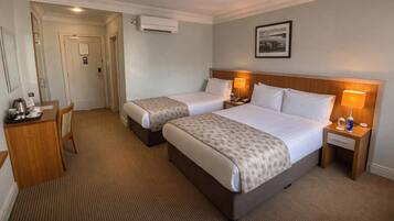 A hotel room with two beds, a desk with a chair, a bedside table with a lamp, and a framed picture on the wall.