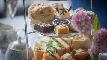 A tiered tray of assorted pastries and desserts, including scones, cakes, and sandwiches, with small bowls of jam and cream.