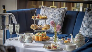 A three-tiered dessert stand with various pastries and sandwiches on a table, a bottle of champagne, and a floral teapot. - Talbot Hotel Stillorgan (Dublin)