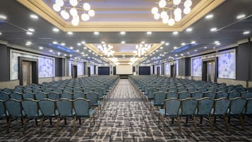 Un salón de conferencias con filas de sillas, una alfombra estampada y un techo con varias luminarias.