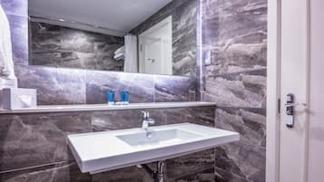 A bathroom with a white sink, marble walls, and a large mirror.