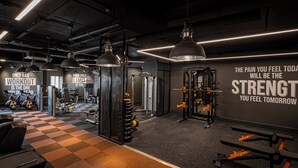 Un gimnasio con equipos de ejercicio variados, texto motivacional en la pared e iluminación colgante.