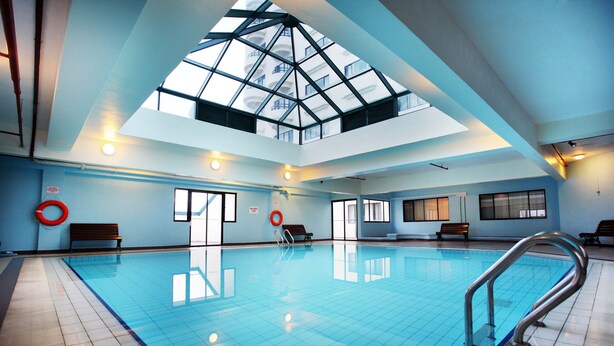 A large indoor swimming pool with a skylight, benches, and lifebuoys. - Copthorne Hotel Cameron Highlands (Brinchang)