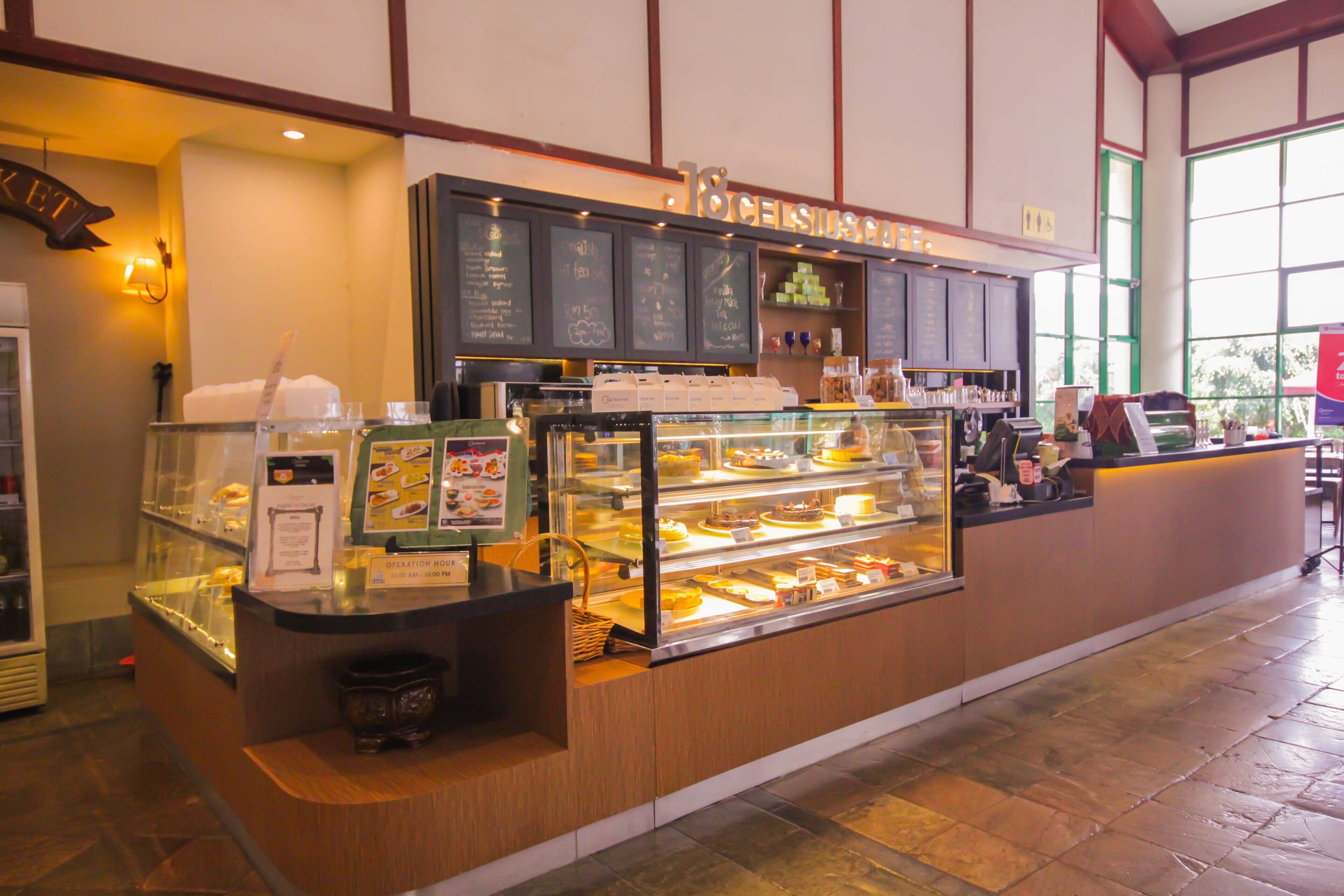 A bakery counter with a display case of pastries, a chalkboard menu, and a seating area with tables and chairs.