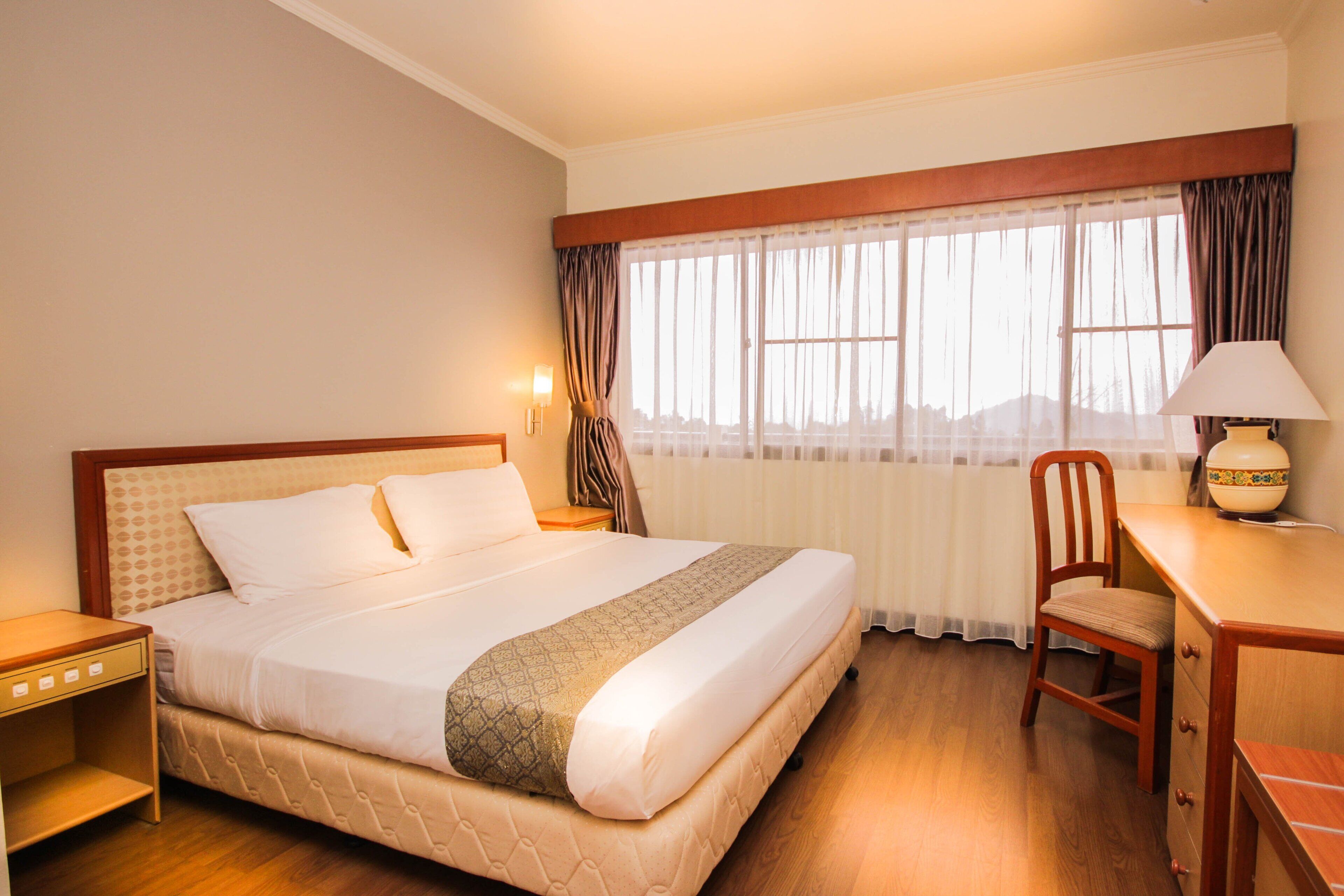 A hotel room with a large bed, a desk, a chair, and a window with curtains.