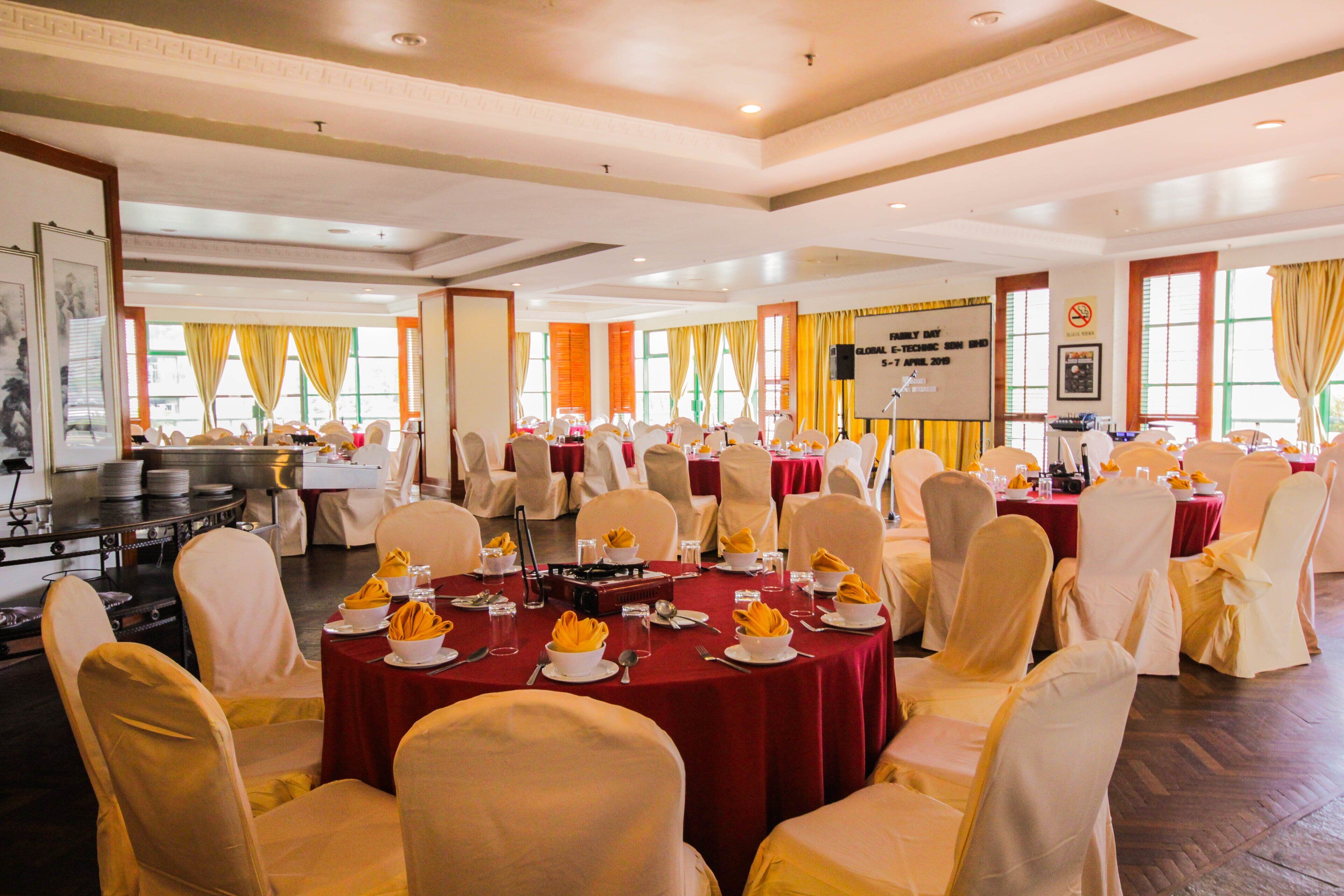 A conference room with round tables, white chairs, and yellow tablecloths.