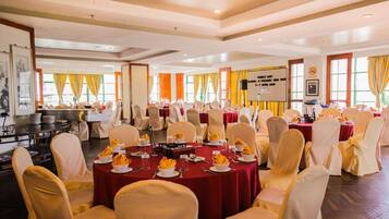 A conference room with round tables, white chairs, and yellow tablecloths.
