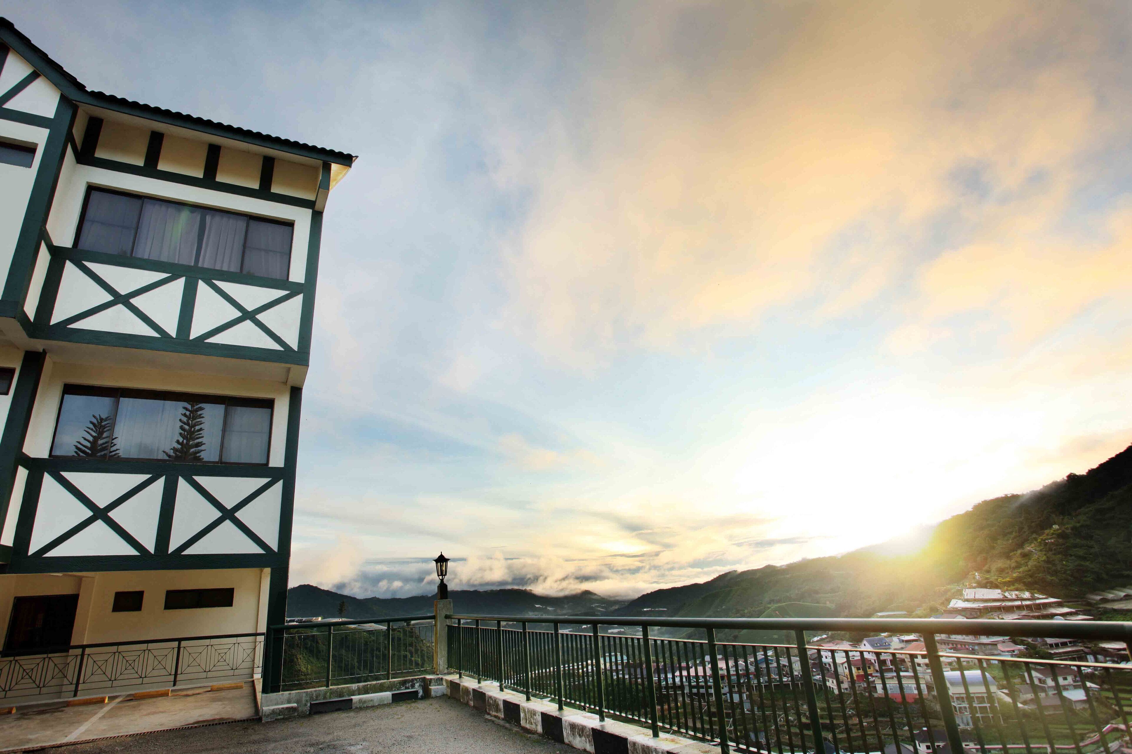 A multi-story building with a balcony, a view of a valley, and a mountain in the background.