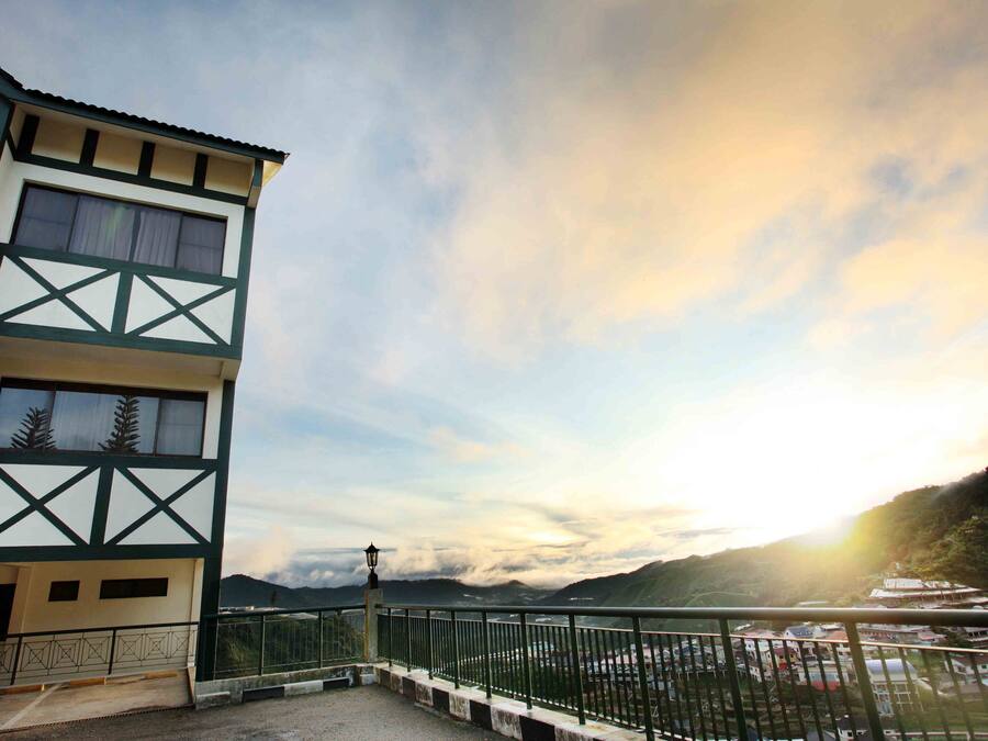 A multi-story building with a balcony, a view of a valley, and a mountain in the background.