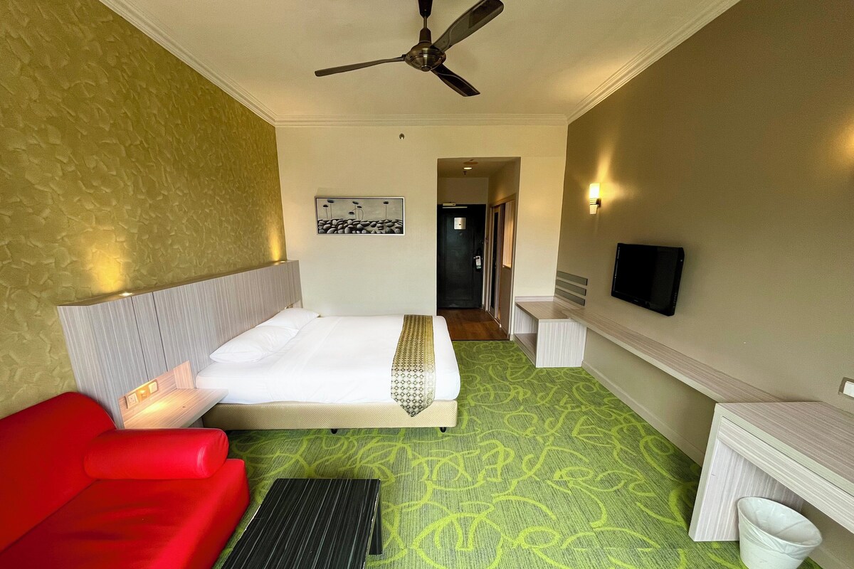 Una habitación de hotel con una cama, un sofá rojo, un escritorio, un ventilador de techo y un televisor.