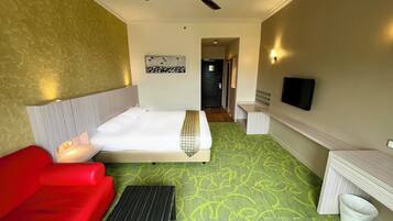 A hotel room with a bed, a red sofa, a desk, a ceiling fan, and a television.