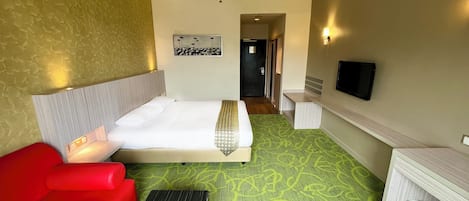 A hotel room with a bed, a red sofa, a desk, a ceiling fan, and a television.