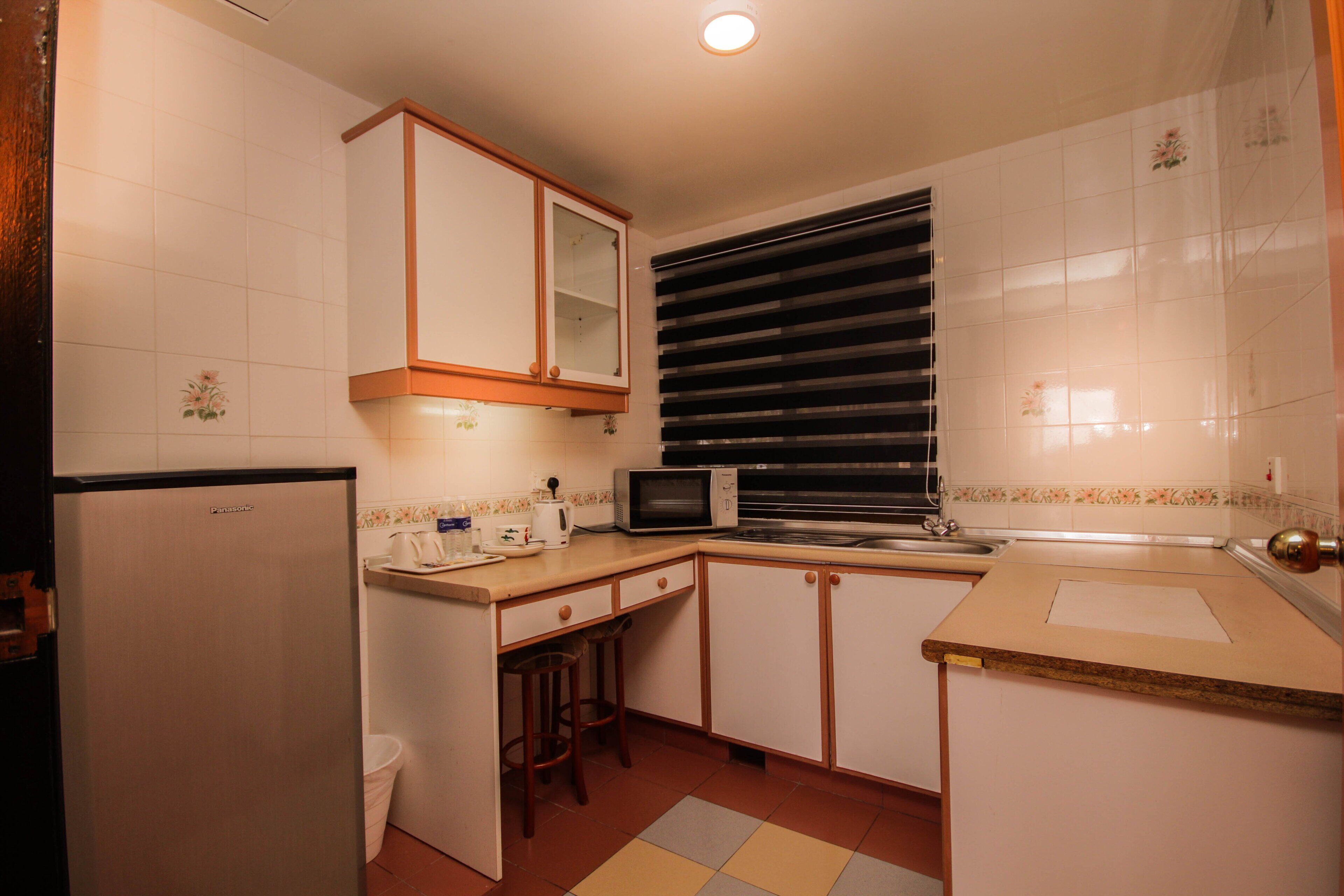 A compact kitchen with a refrigerator, microwave, sink, and a window with blinds.
