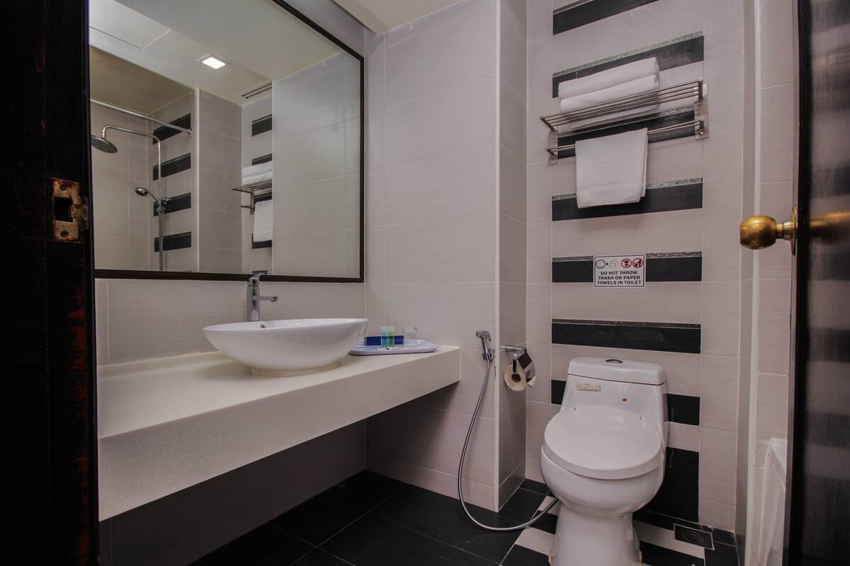 A modern bathroom with a white sink, a large mirror, a toilet, and a towel rack.