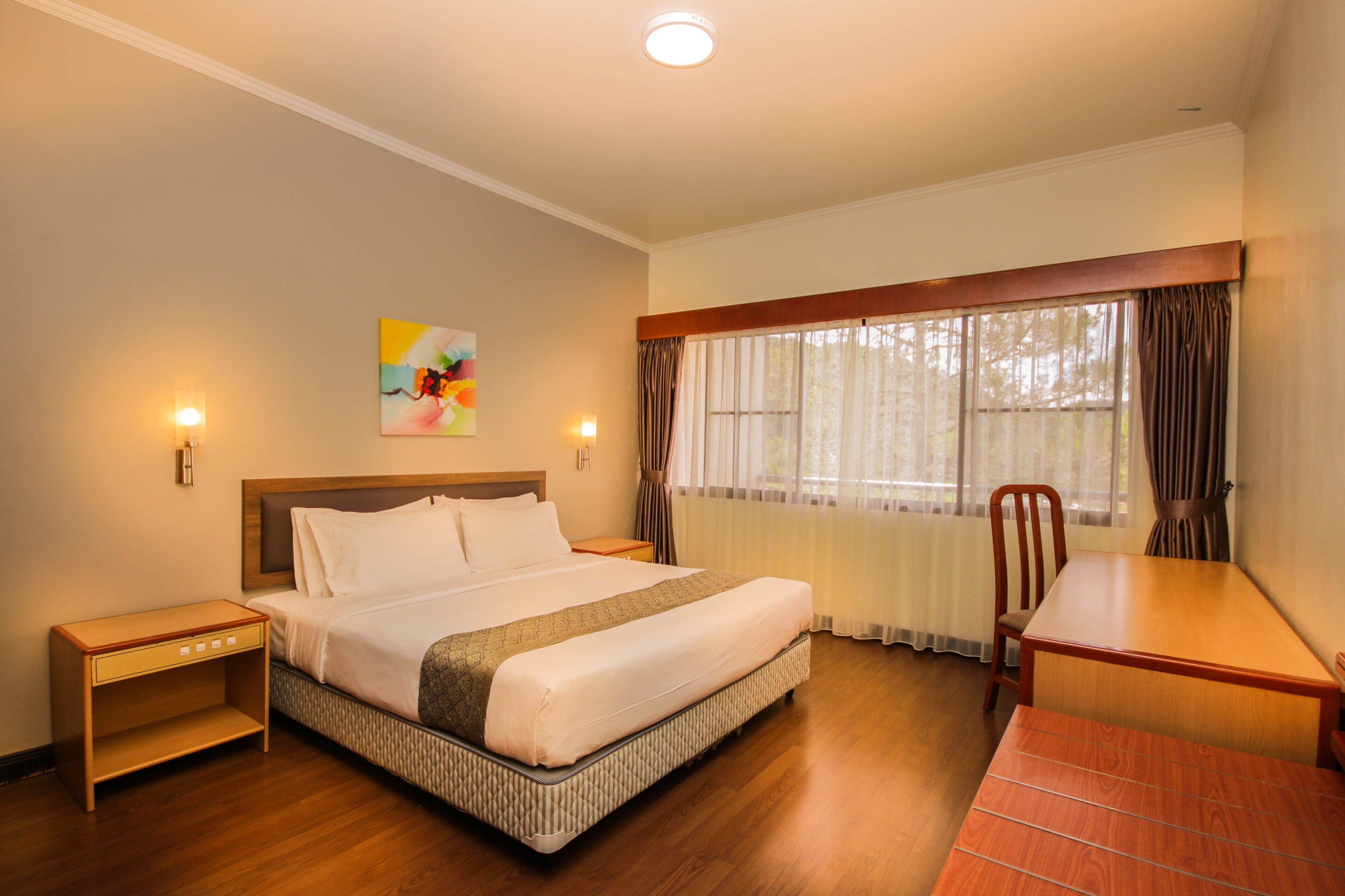 A hotel room with a bed, bedside table, chair, and a desk.