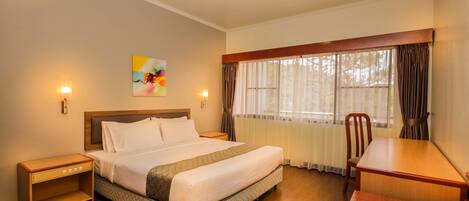 A hotel room with a bed, bedside table, chair, and a desk.