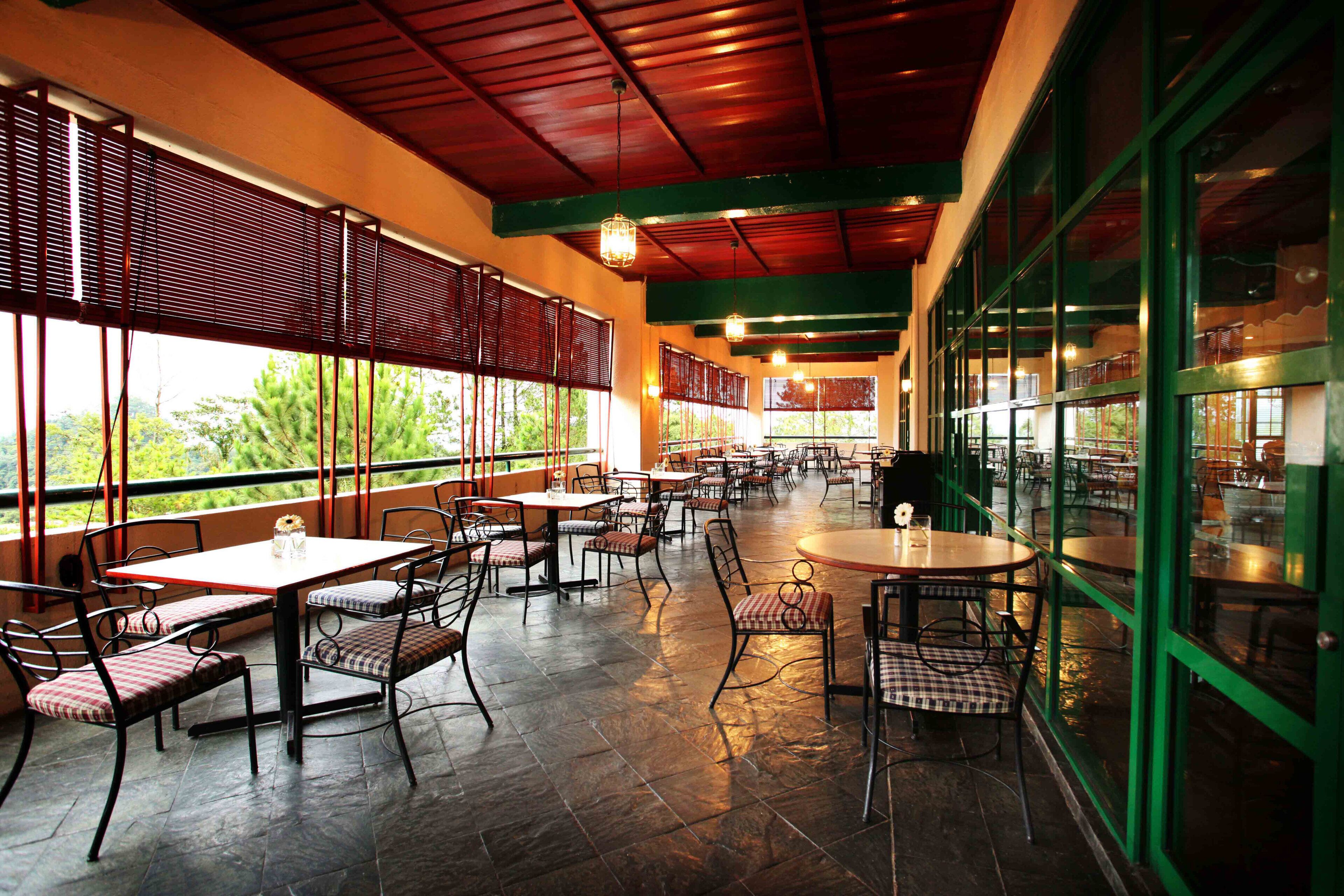 An indoor dining area with tables and chairs, large windows, and a view of greenery outside.
