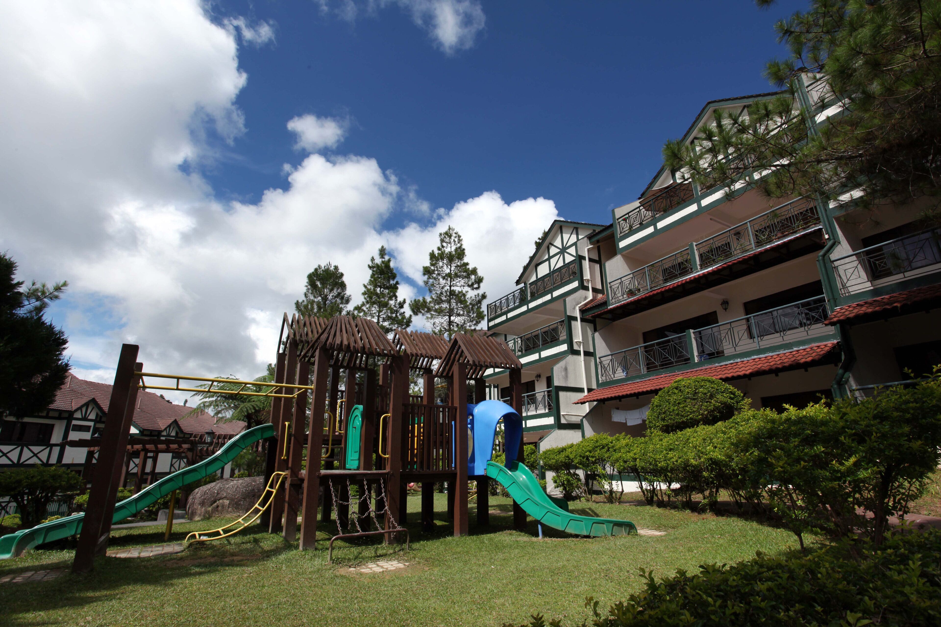A playground with slides and climbing structures, surrounded by well-maintained grass and trees, with a building in the background.