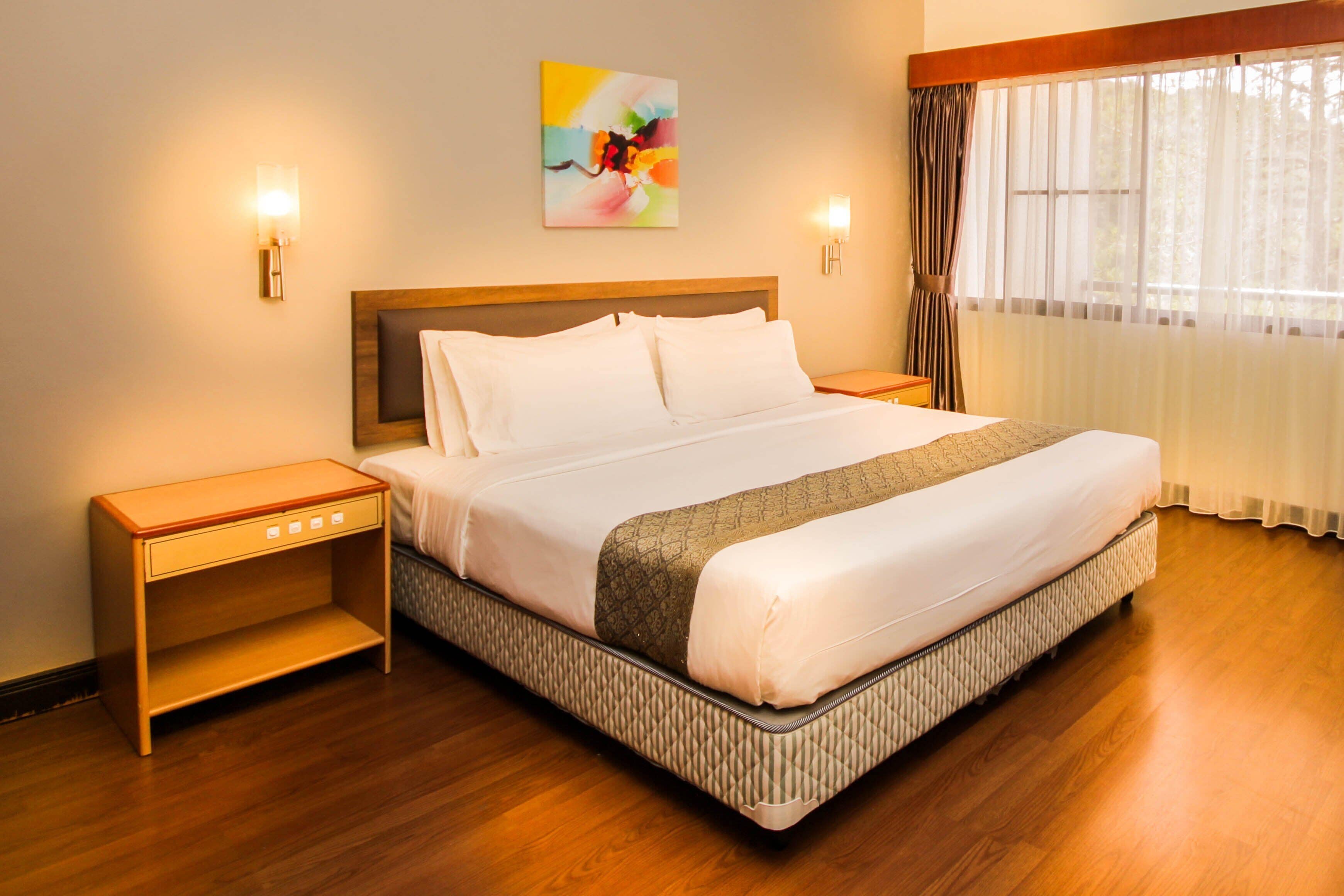 A neatly made bed with a wooden headboard, two bedside tables, and a large window with sheer curtains.