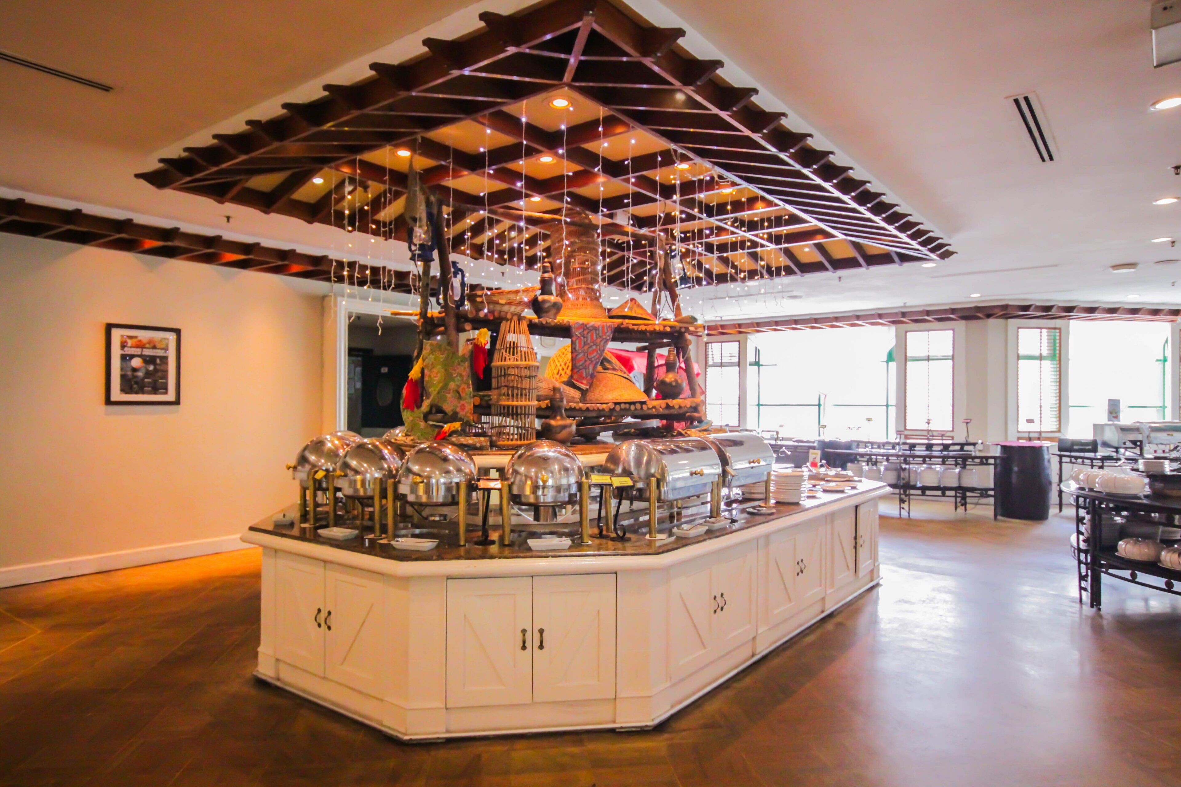 Una habitación amplia con una isla central grande, equipada con diversos electrodomésticos de cocina y una estructura decorativa en el techo.