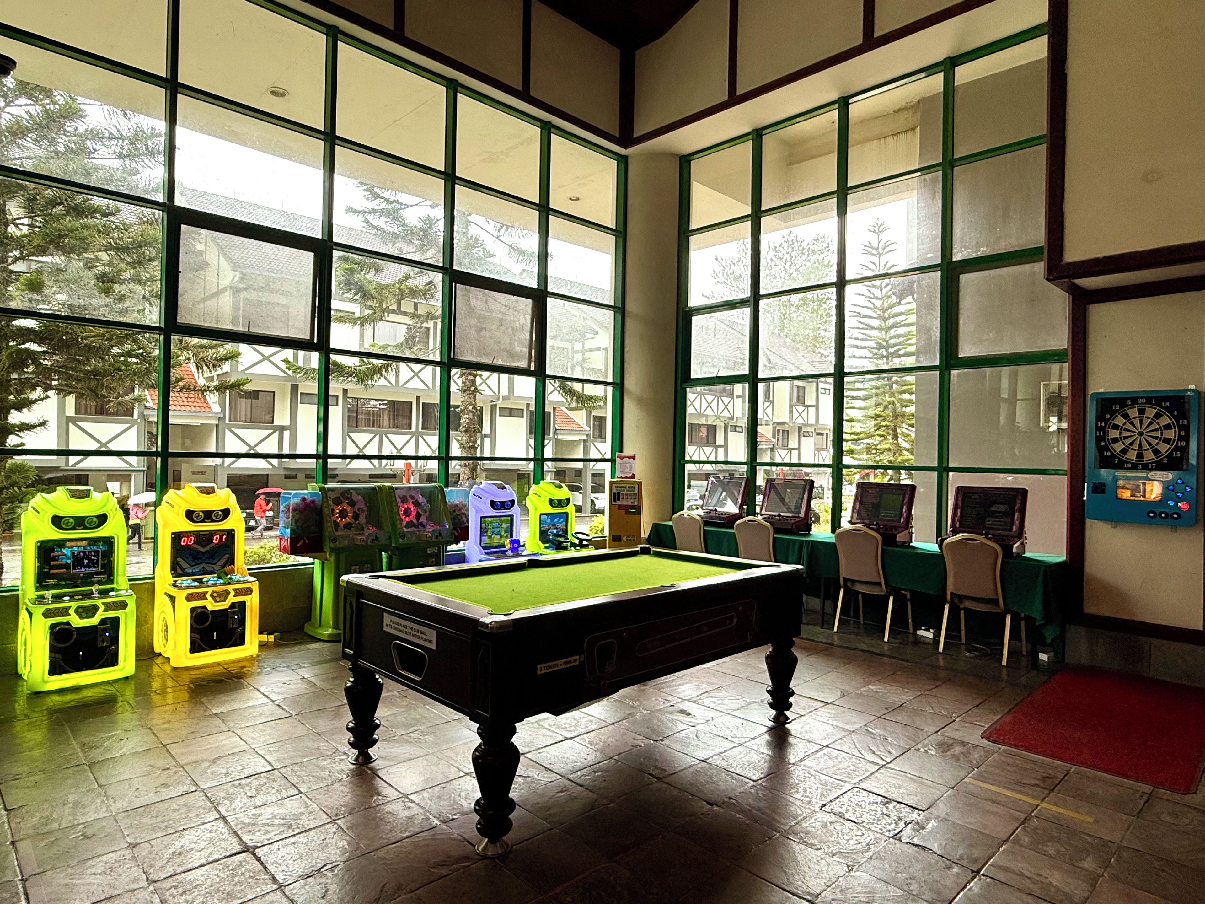 A billiards room with a pool table, multiple arcade machines, and large windows.