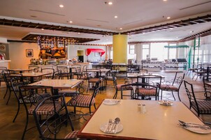 Un comedor amplio con varias mesas y sillas, una barra al fondo y ventanas grandes que dejan entrar luz natural.