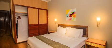 Habitación de hotel con cama, armario de madera, mesitas de noche y un cuadro abstracto de colores en la pared.