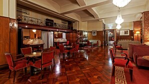 A spacious hotel lobby with a high ceiling, wooden flooring, and a variety of seating arrangements including red upholstered chairs and a striped sofa. - Hotel Astoria (Coimbra)