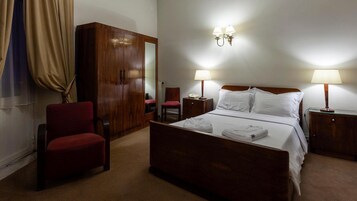 Habitación de hotel con cama, dos mesitas de noche, armario, una silla y dos lámparas de pared.