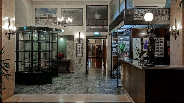 A lobby with a glass partition, a reception desk, and a chandelier. - Hotel Astoria (Coimbra)
