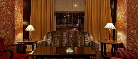 Una habitación con sofá, dos lámparas, una mesa y una ventana con cortinas.