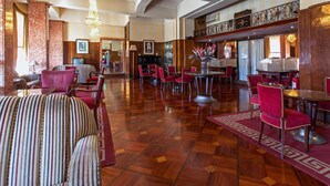 A spacious lobby with a checkered floor, red upholstered chairs, and a central round table. - Hotel Astoria (Coimbra)