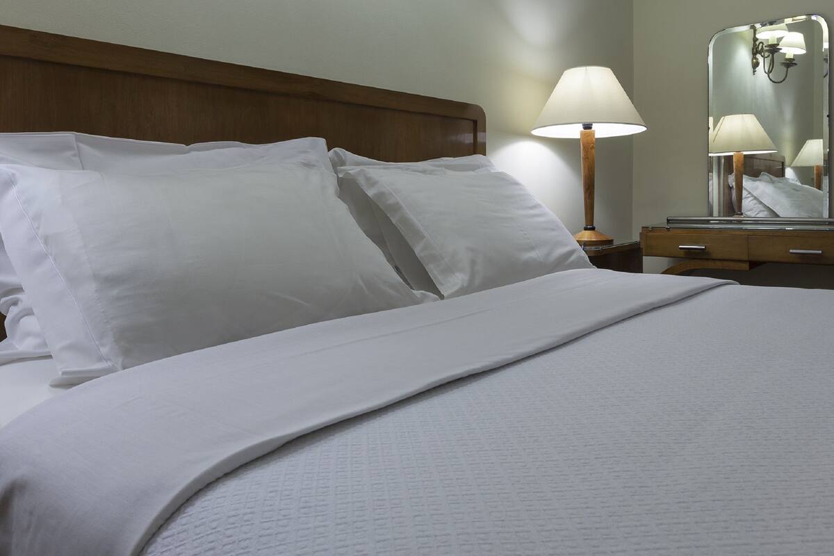 A neatly made bed with white linens, a wooden headboard, and a bedside table with a lamp.