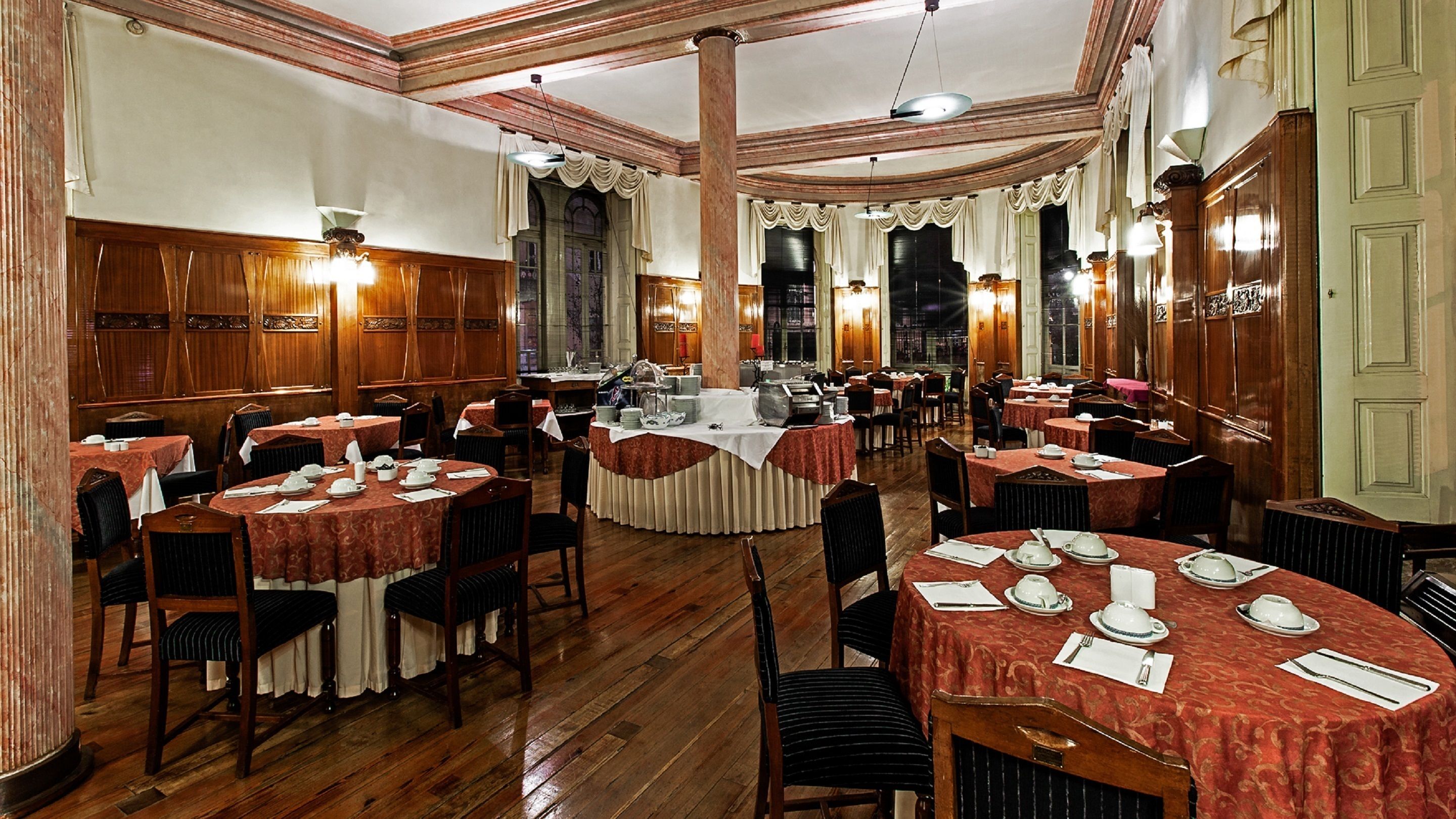 Un amplio salón de banquetes con mesas redondas dispuestas para comer, paneles de madera y candelabros.