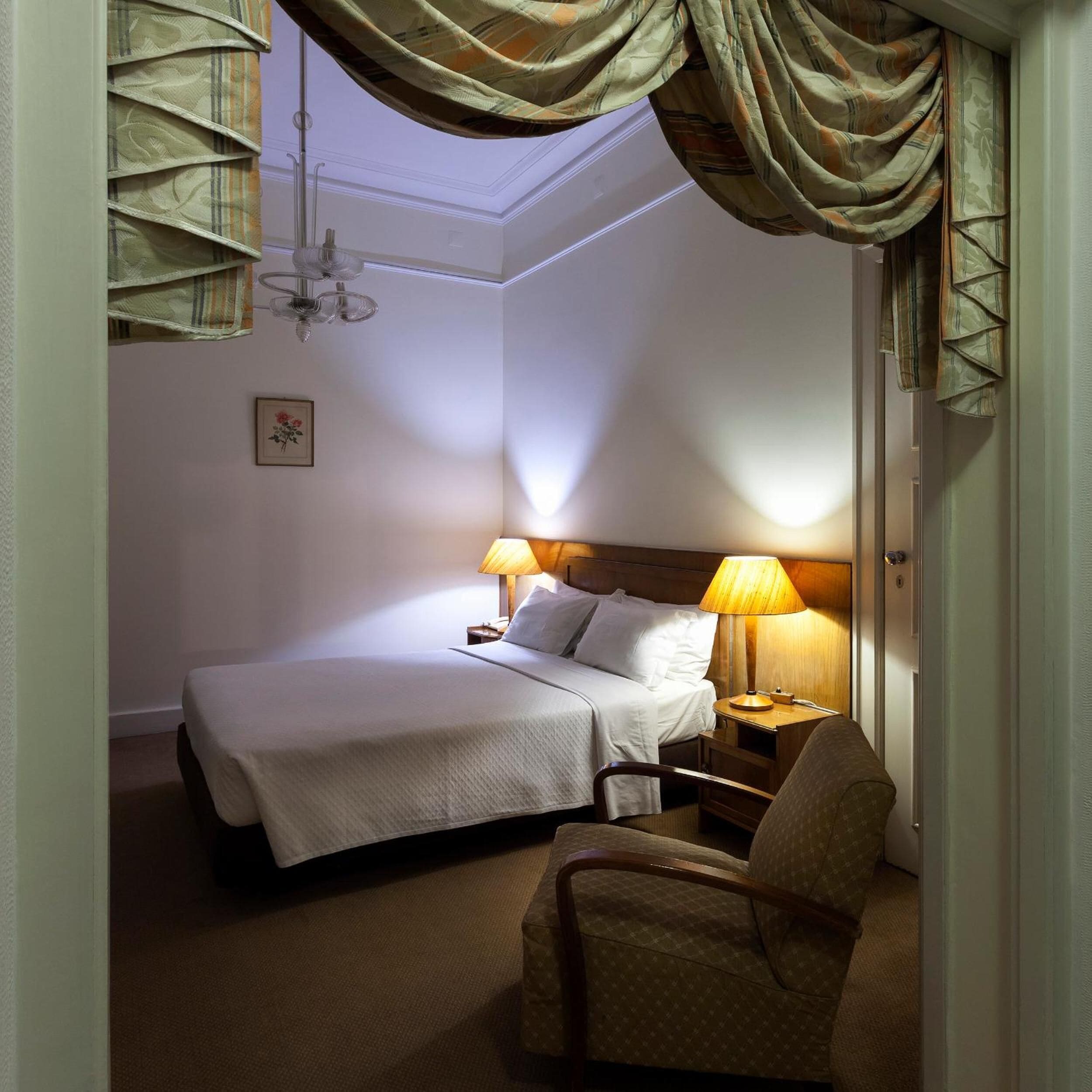 A neatly arranged hotel room with a bed, bedside lamps, a chair, and a framed picture on the wall.