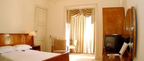 A hotel room with a bed, a chair, a desk with a television, and a mirror.