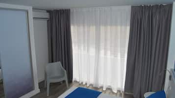 A hotel room with a bed, a chair, a window with curtains, and a sliding door.