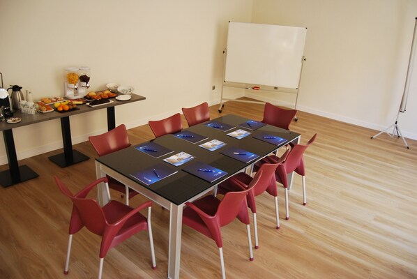 Una sala de conferències amb una taula llarga, cadires vermelles, una pissarra i un bufet amb fruita i begudes.