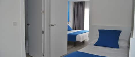 Une chambre d’hôtel avec deux lits, chacun agrémenté de draps bleus et blancs, et une porte donnant sur une autre pièce.
