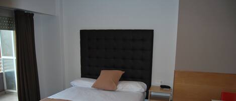 Habitación de hotel con una cama, una mesita de noche con teléfono y una pequeña mesa de madera con sillas.