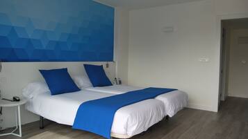 A double bed with white and blue bedding, a small bedside table with a lamp, and a blue geometric wall design.