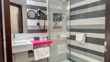 A modern bathroom with a glass-enclosed shower, a vanity with a pink countertop, and striped wall tiles.