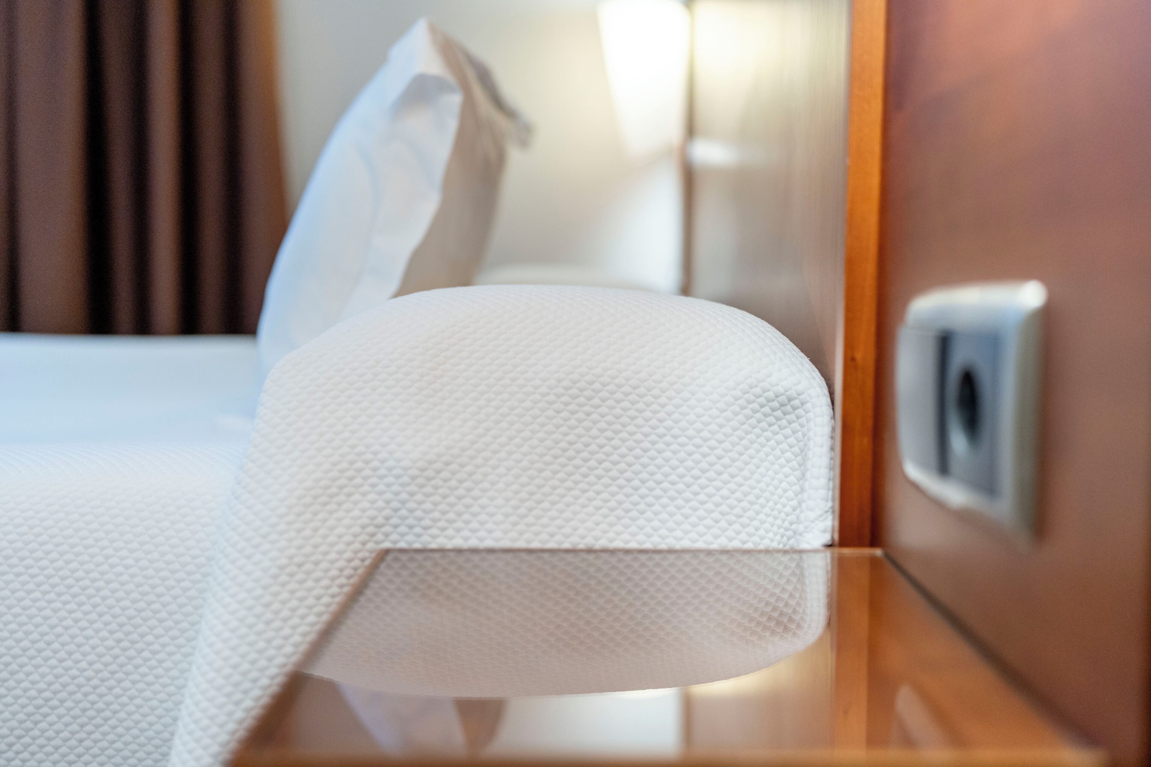 Une chambre d’hôtel avec un lit bien fait, une table de chevet avec une boîte de mouchoirs et une prise électrique au mur.