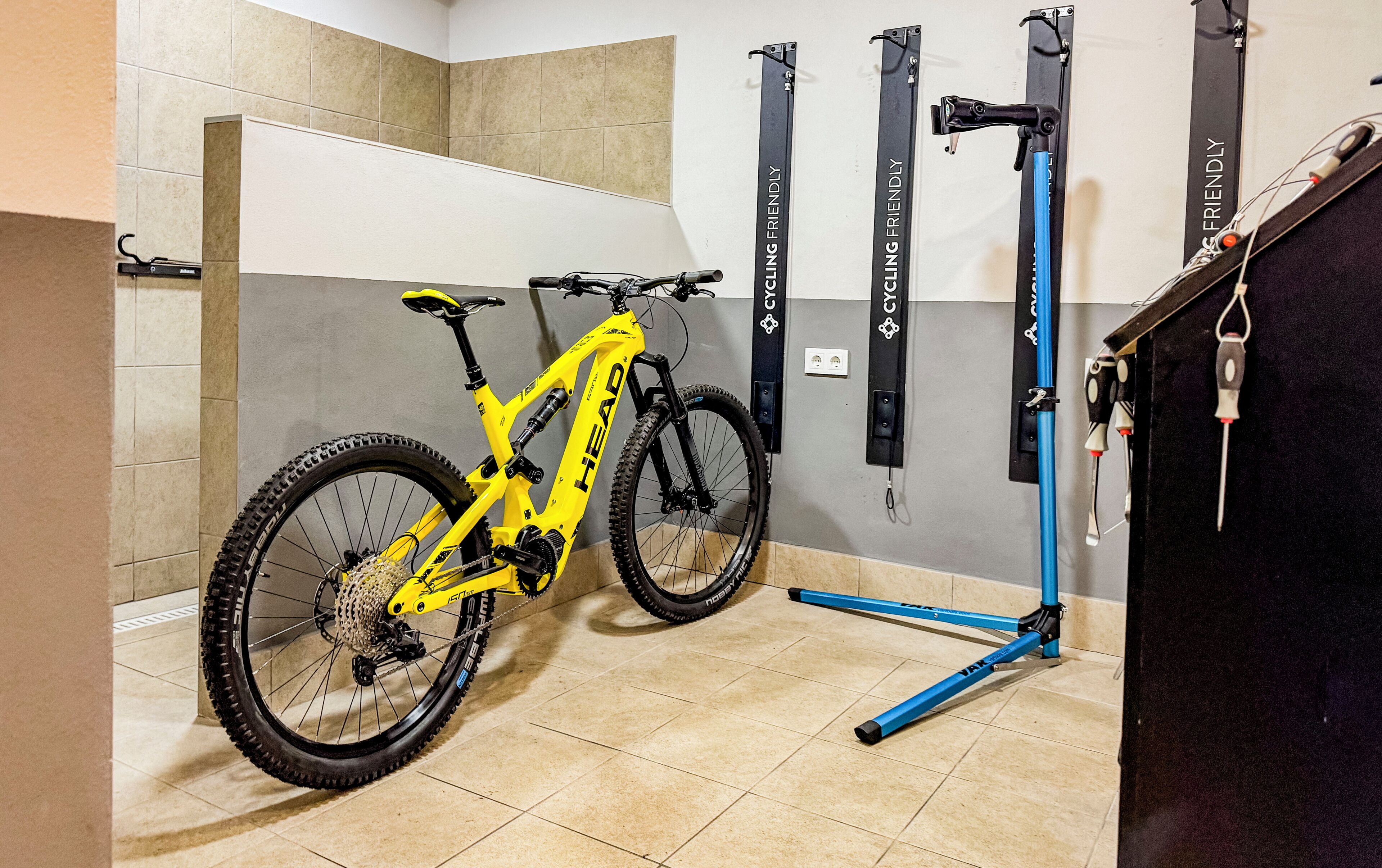 Een mountainbike in een hoek, met een fietsenrek aan de muur en een blauwe opklapbare fiets standaard.