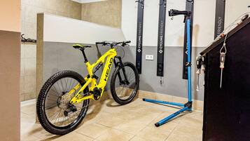 Een mountainbike in een hoek, met een fietsenrek aan de muur en een blauwe opklapbare fiets standaard.
