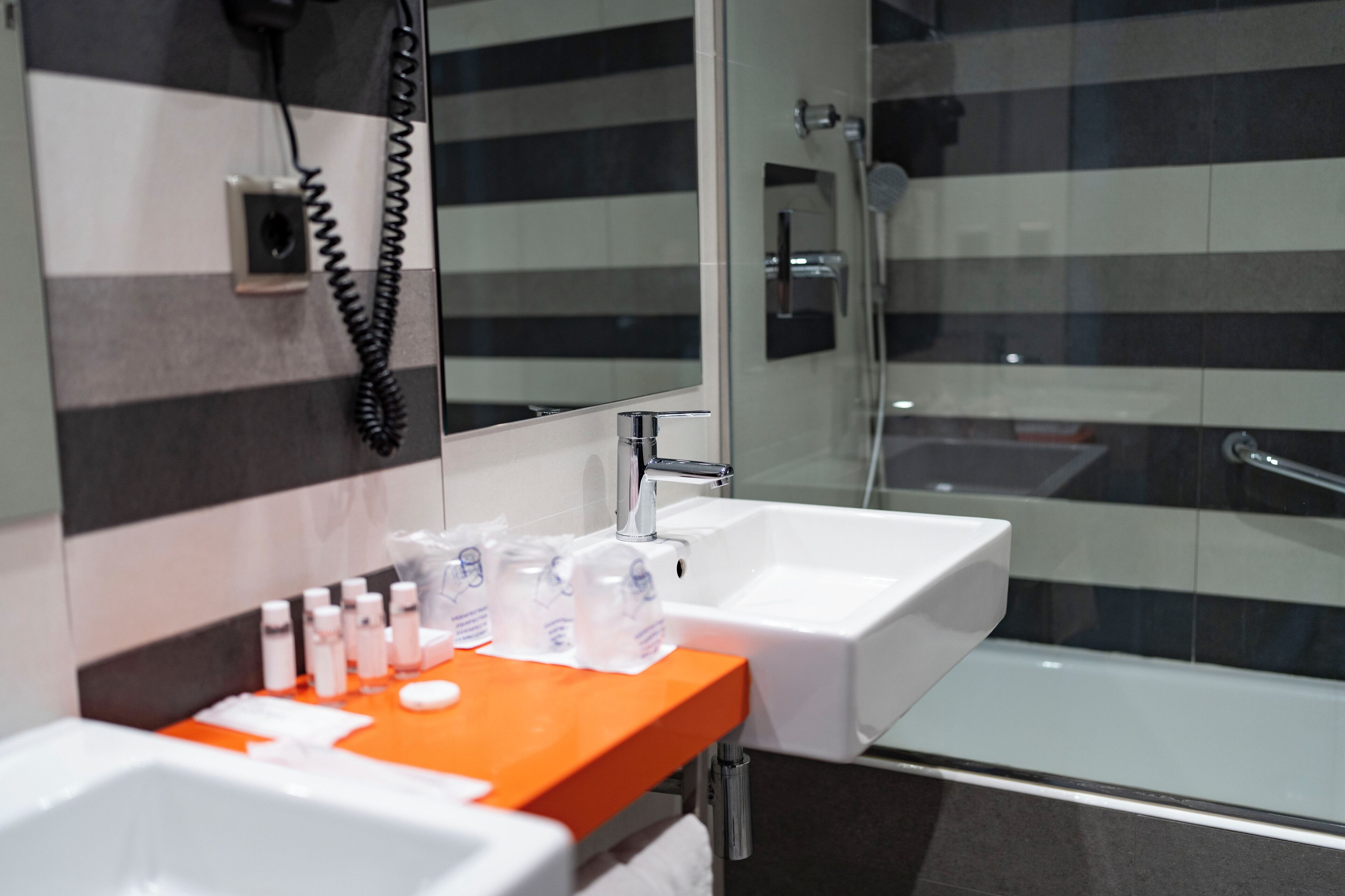A modern bathroom with two sinks, a glass shower enclosure, and a telephone mounted on the wall.